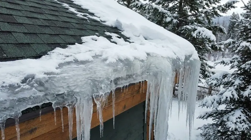 Thick ice dam and icicles built up along the eave of a snow-covered roof